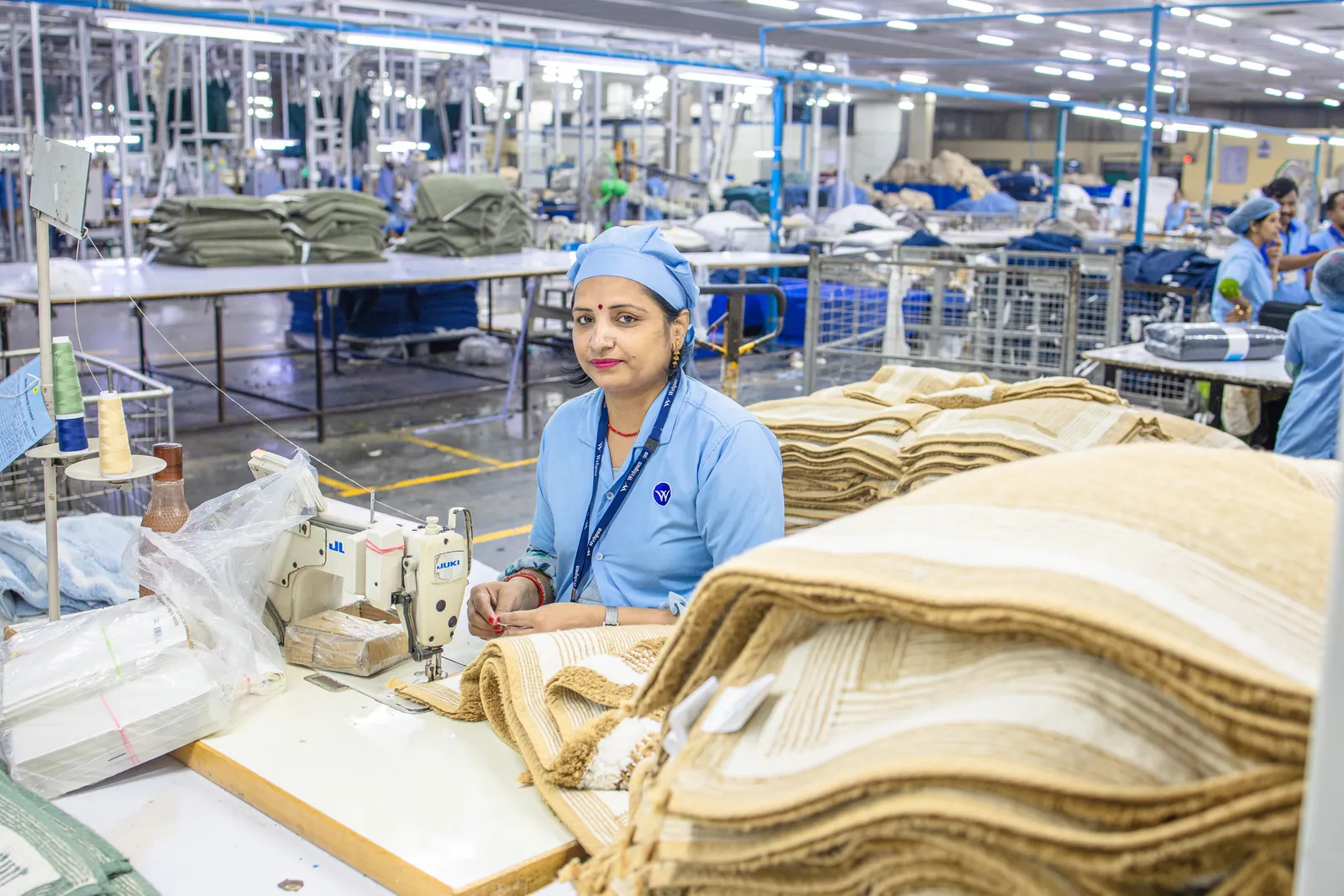 Production worker in a blue uniform with stacks of finished goods on a factory floor in India