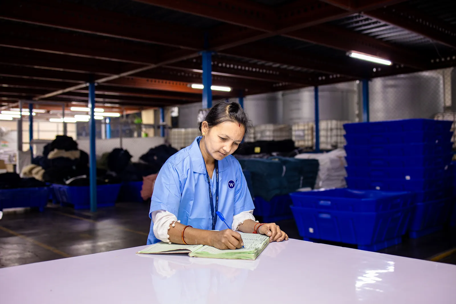 Supervisor in a blue uniform recording details at a workstation in an Indian warehouse