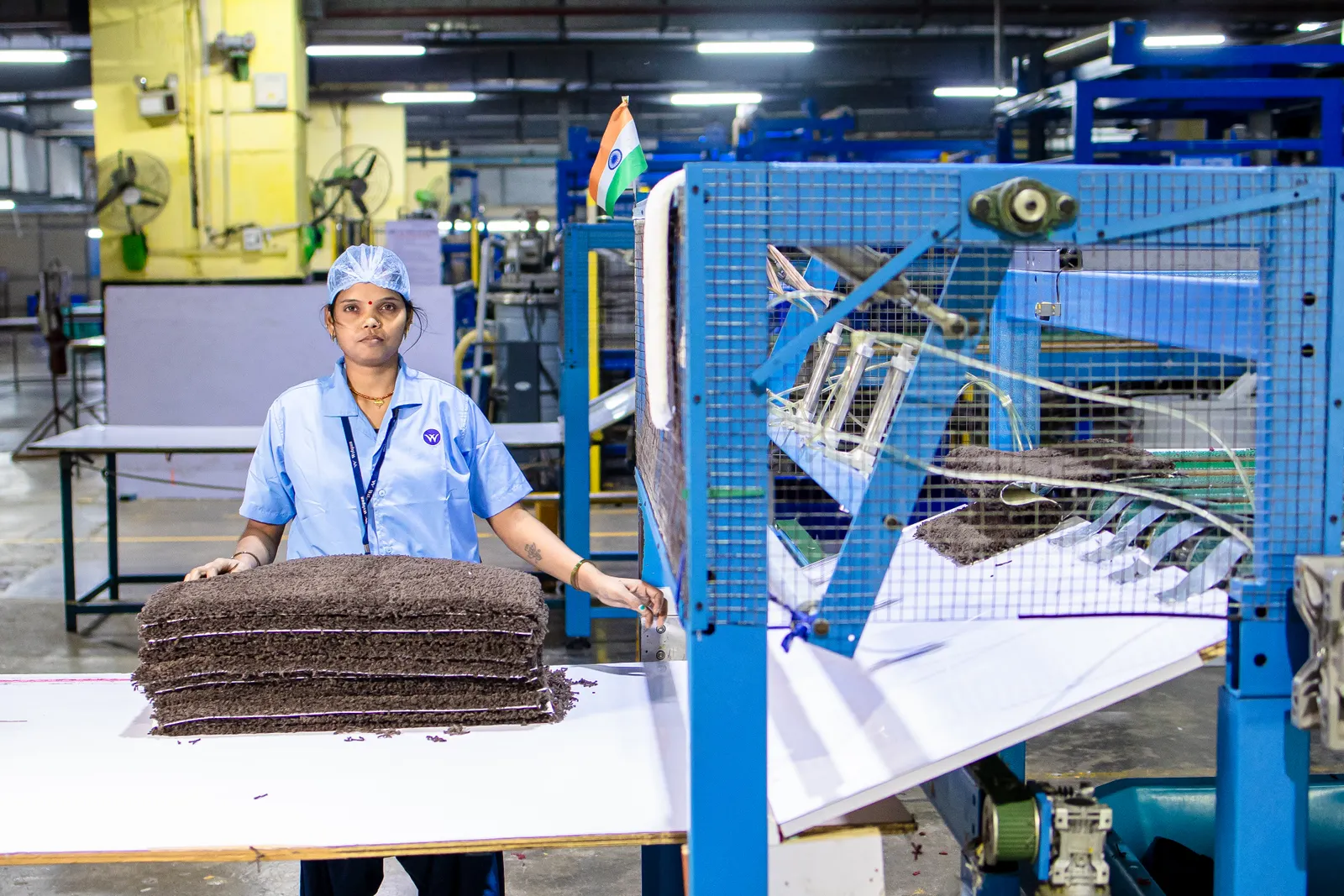 Factory worker in a blue uniform handling finished material at a production machine in India