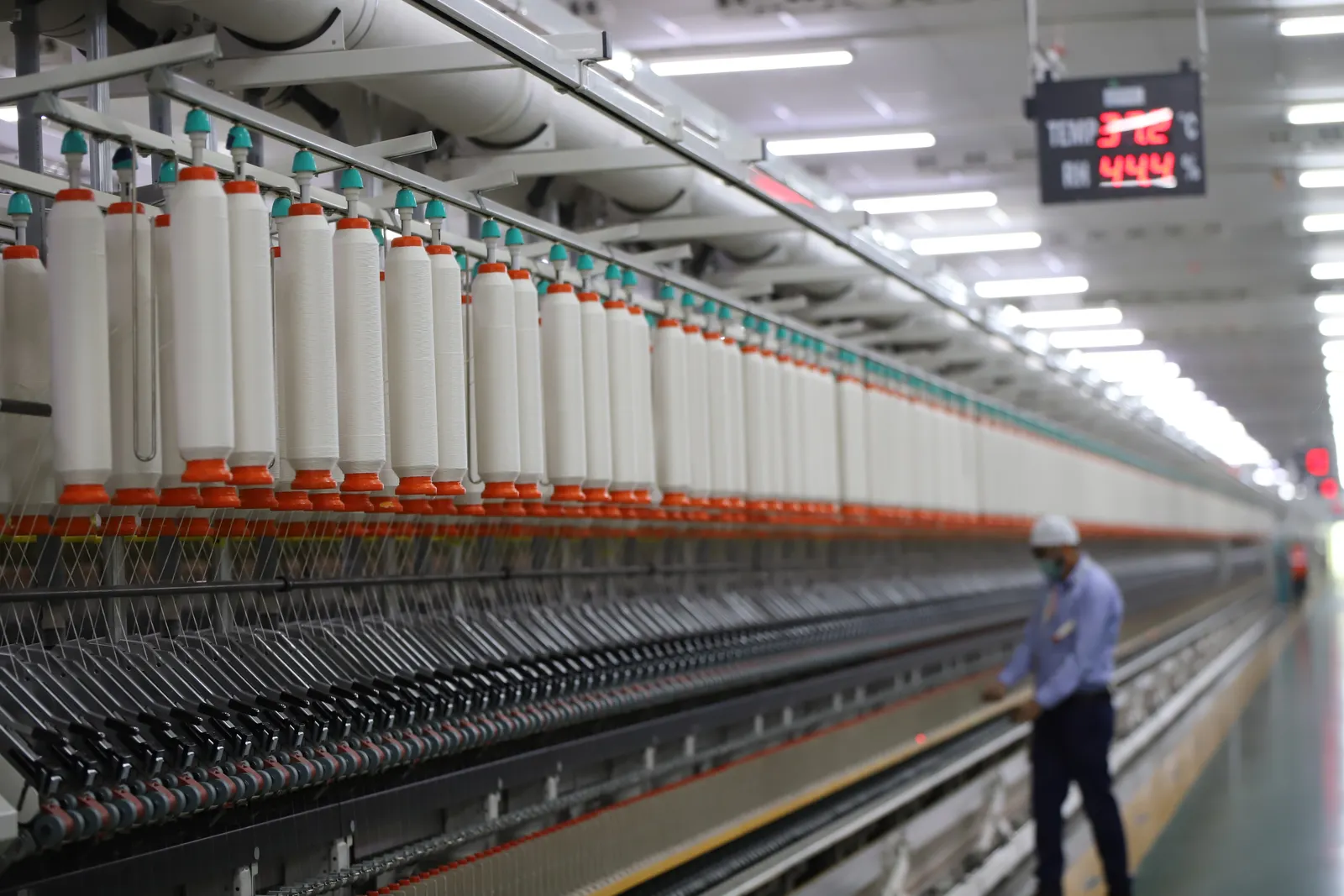Worker walking along a long row of spinning machines in a modern mill in New Delhi